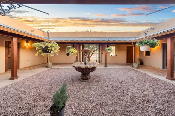 Courtyard with terracotta walls, gravel ground, ornamental fountain, hanging plants, and sunset sky overhead