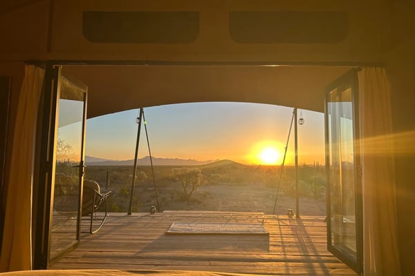 Sunset view from open glass doors onto wooden deck with swing, overlooking desert landscape and mountains